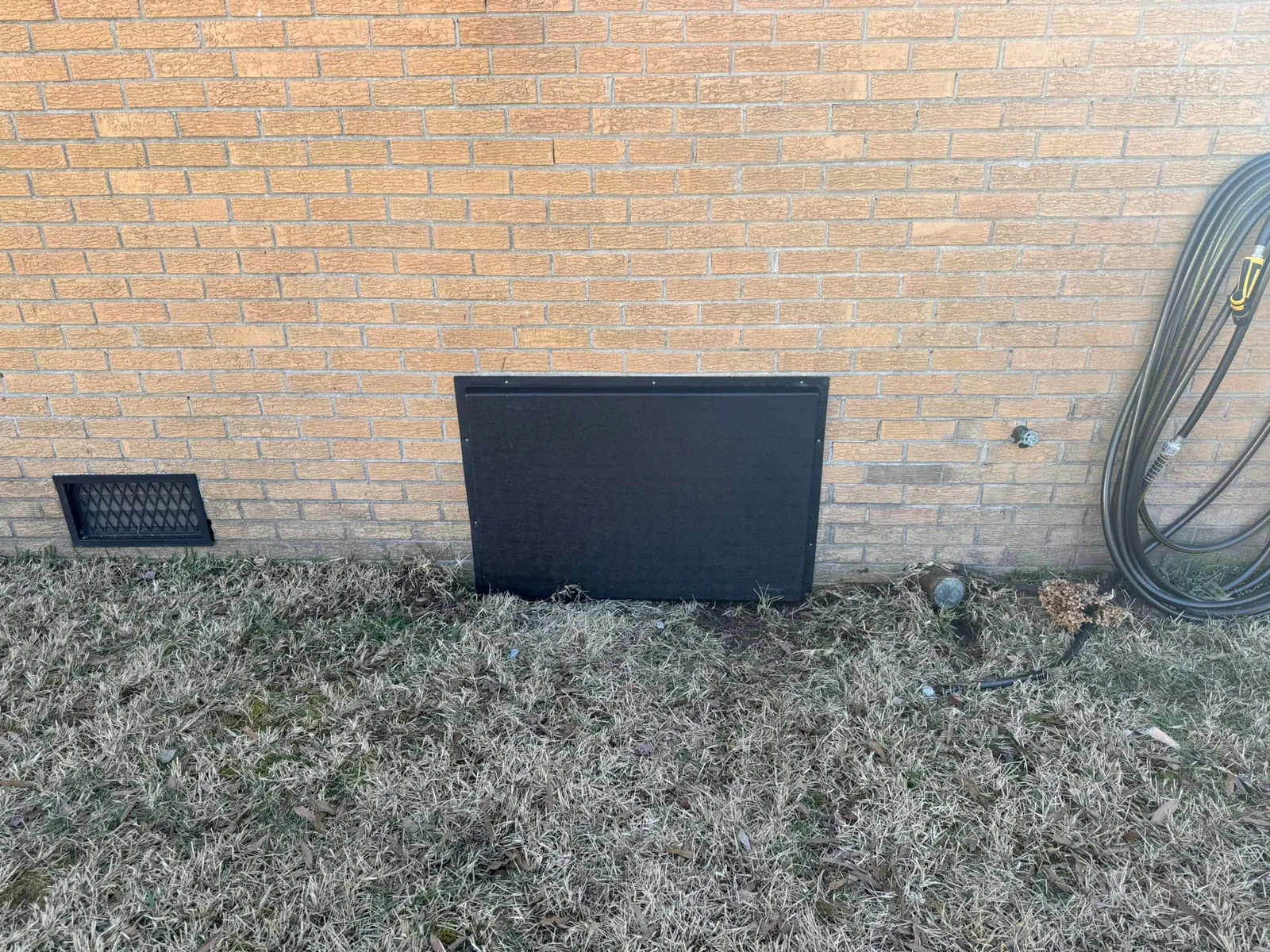New dark crawlspace access door installed in a brick foundation wall