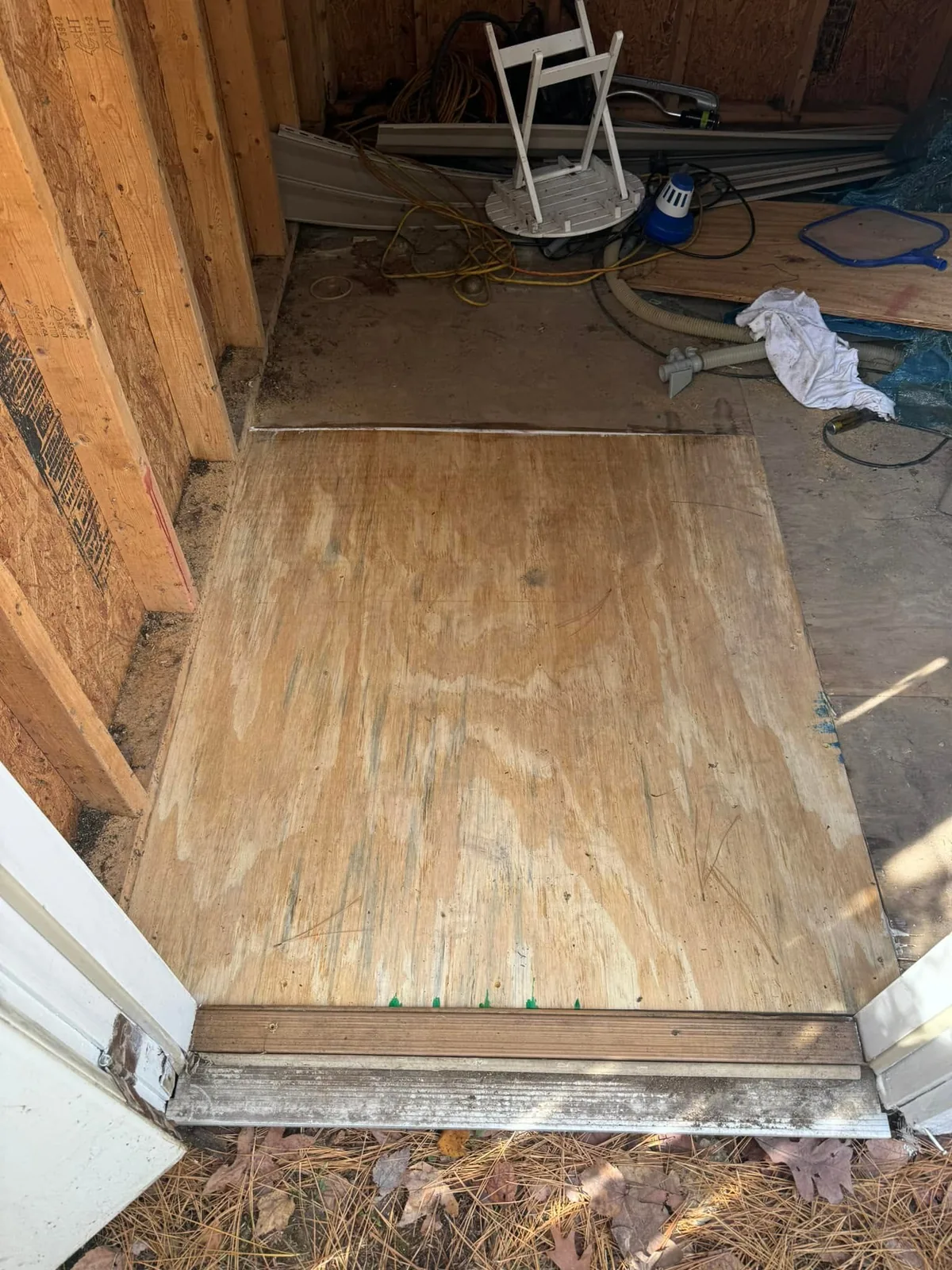Replacement plywood floor section at a shed entrance, with the surrounding original floor visible