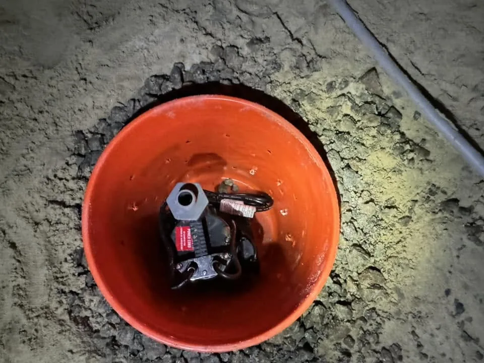 Small sump pump positioned inside an orange basin in a crawlspace during installation